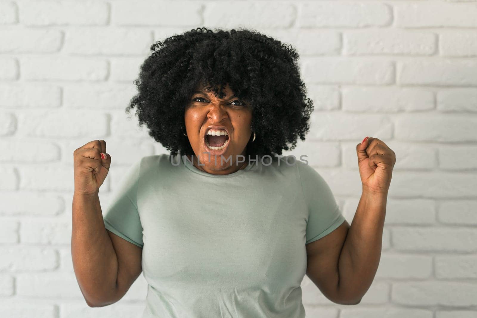 Angry african american woman screaming on brick background. Bad aggressive emotions and premenstrual syndrome or pms