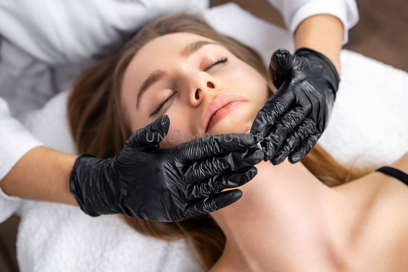 A lovely young woman relaxes during her face lifting massage session at the beauty salon.