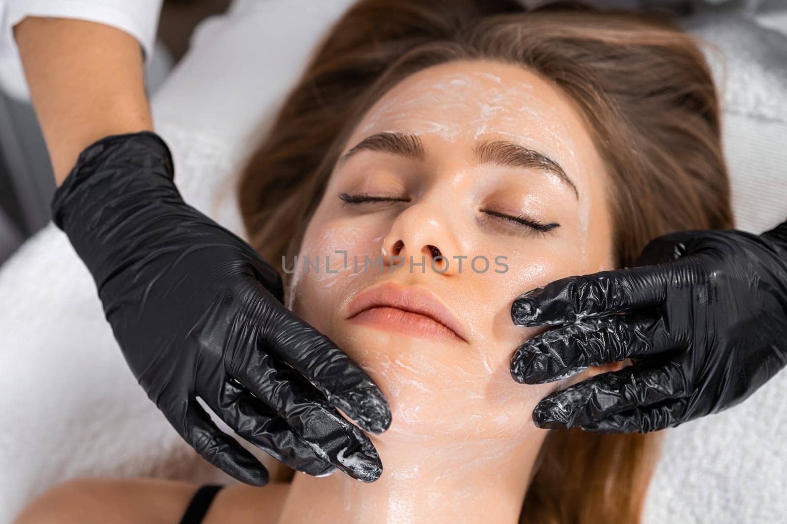 Young blonde woman getting face massage treatment at cosmetology clinic. Skin and body care concept.