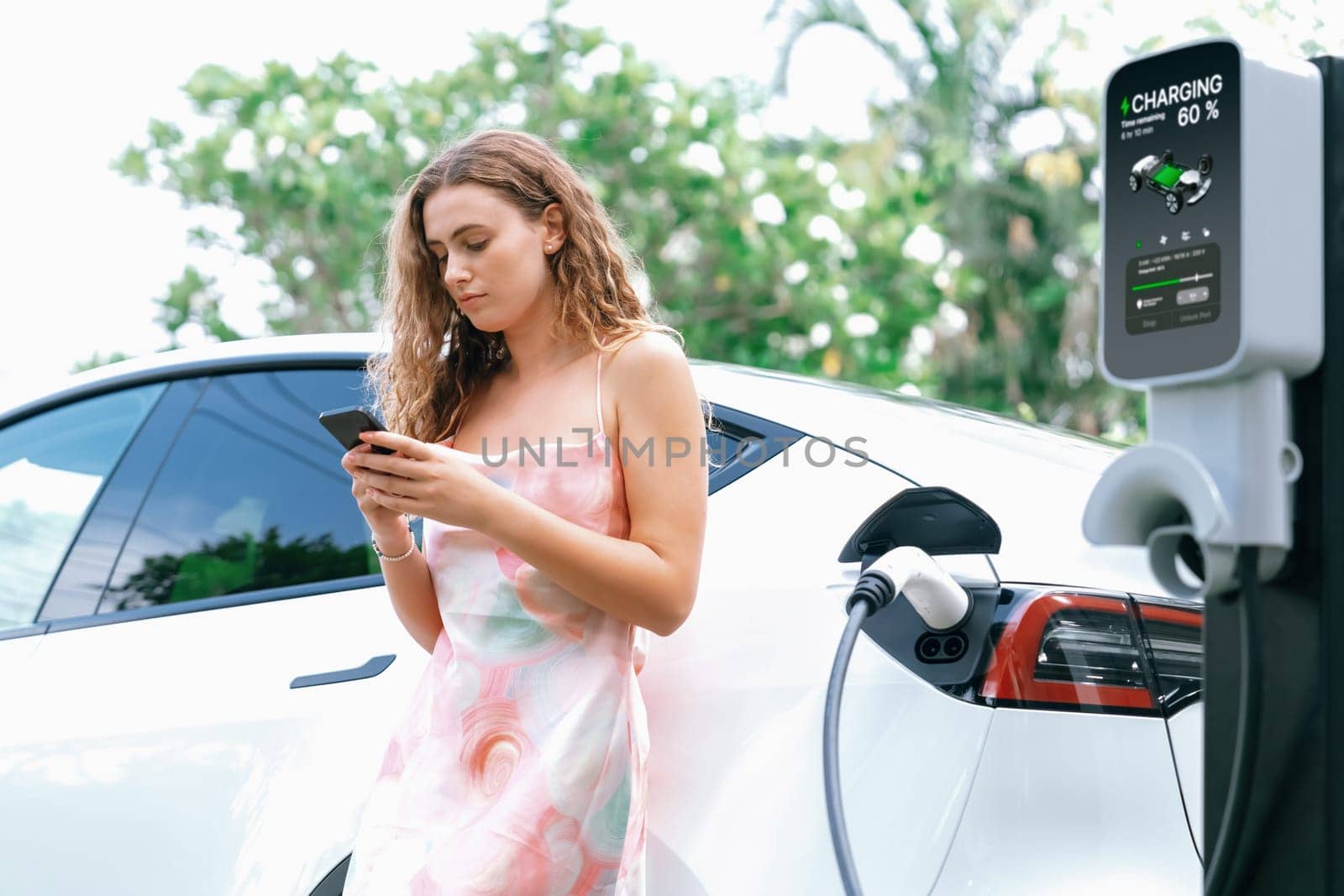 Modern eco-friendly woman recharging electric vehicle from EV charging station. Innovative EV technology utilization for tracking energy usage to optimize battery charging. Synchronos