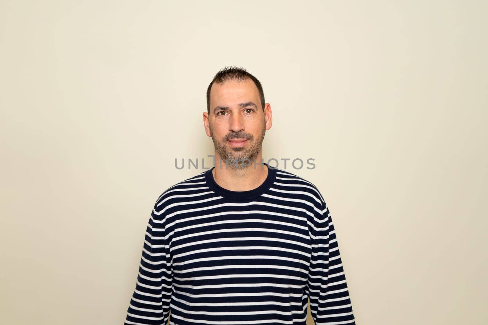 Hispanic man with beard wearing a striped sweater posing smiling on beige studio background. by Barriolo82