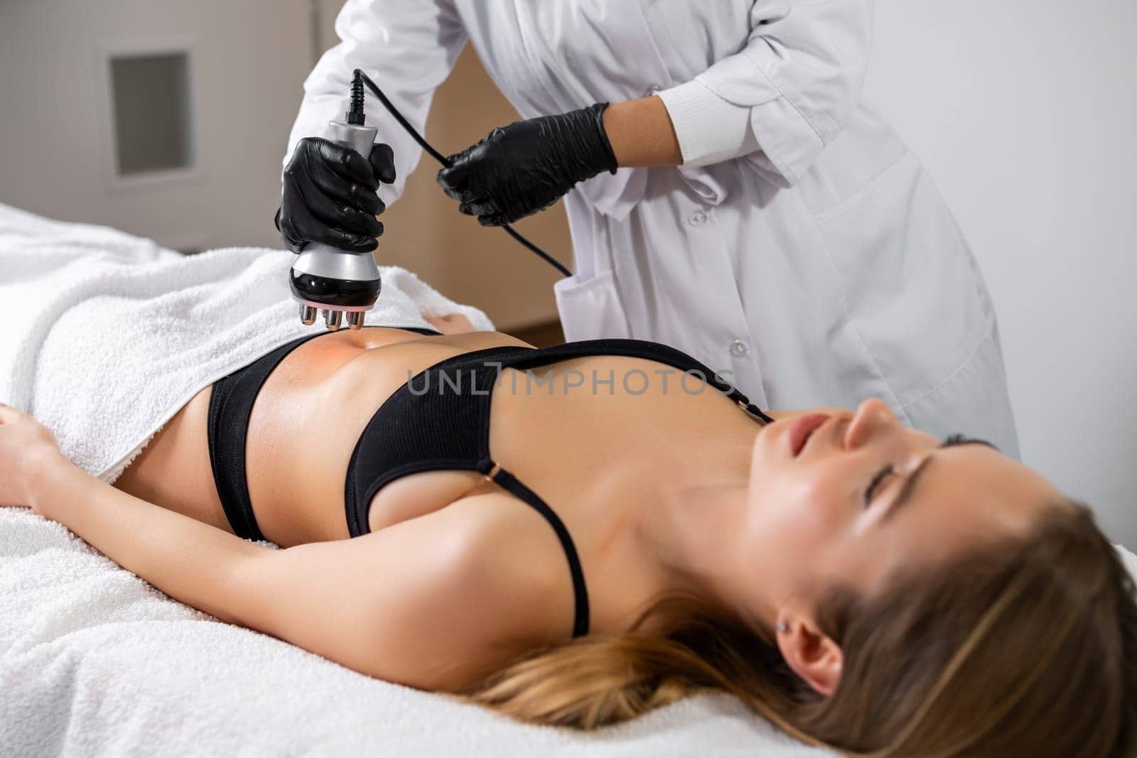 Young woman is lying while getting RF lifting of the body in a spa beauty salon