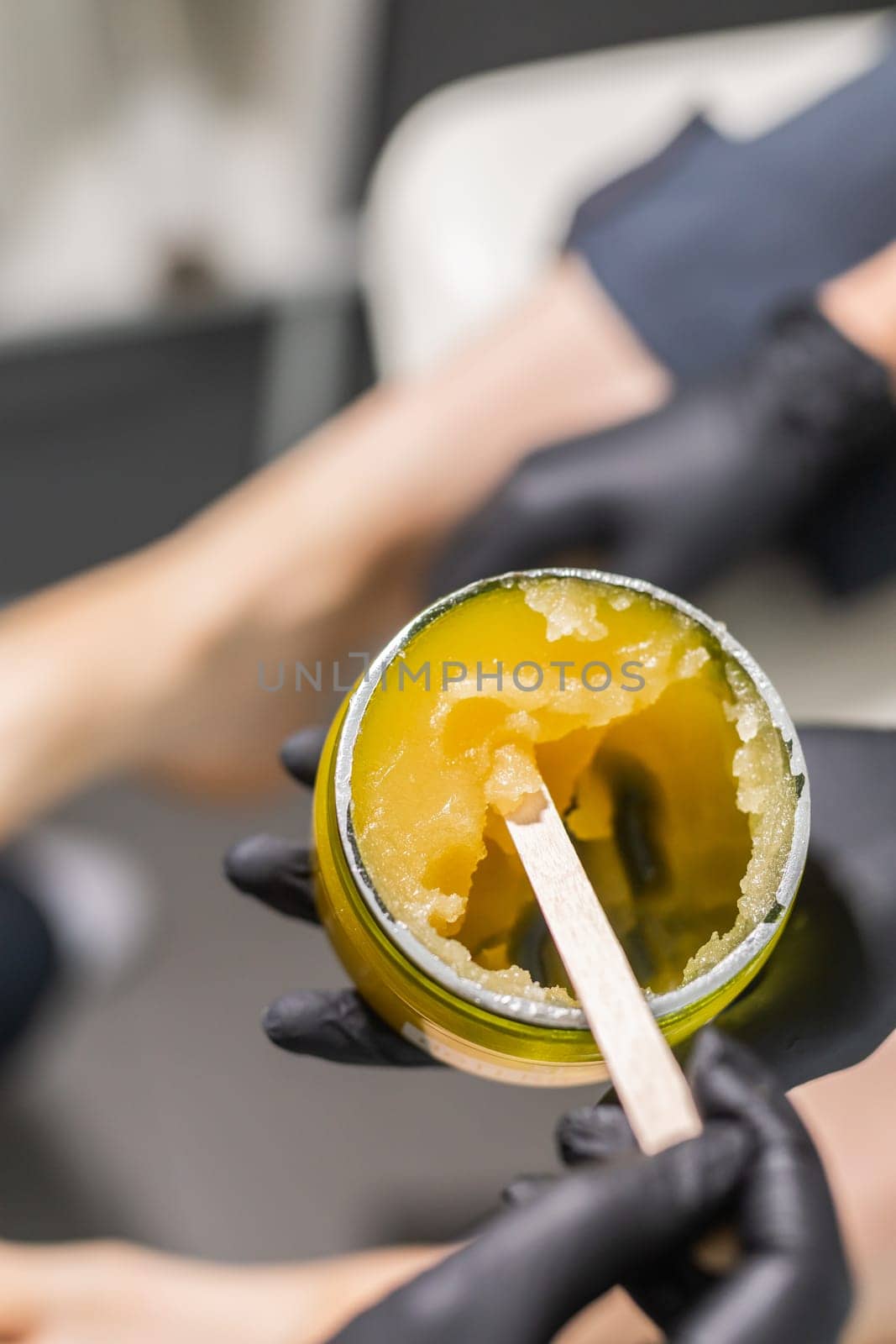 Orange body scrub with sugar and oil in glass jar in female hand. Homemade cosmetic for peeling and spa care. Copy space and empty place for advertising by Satura86