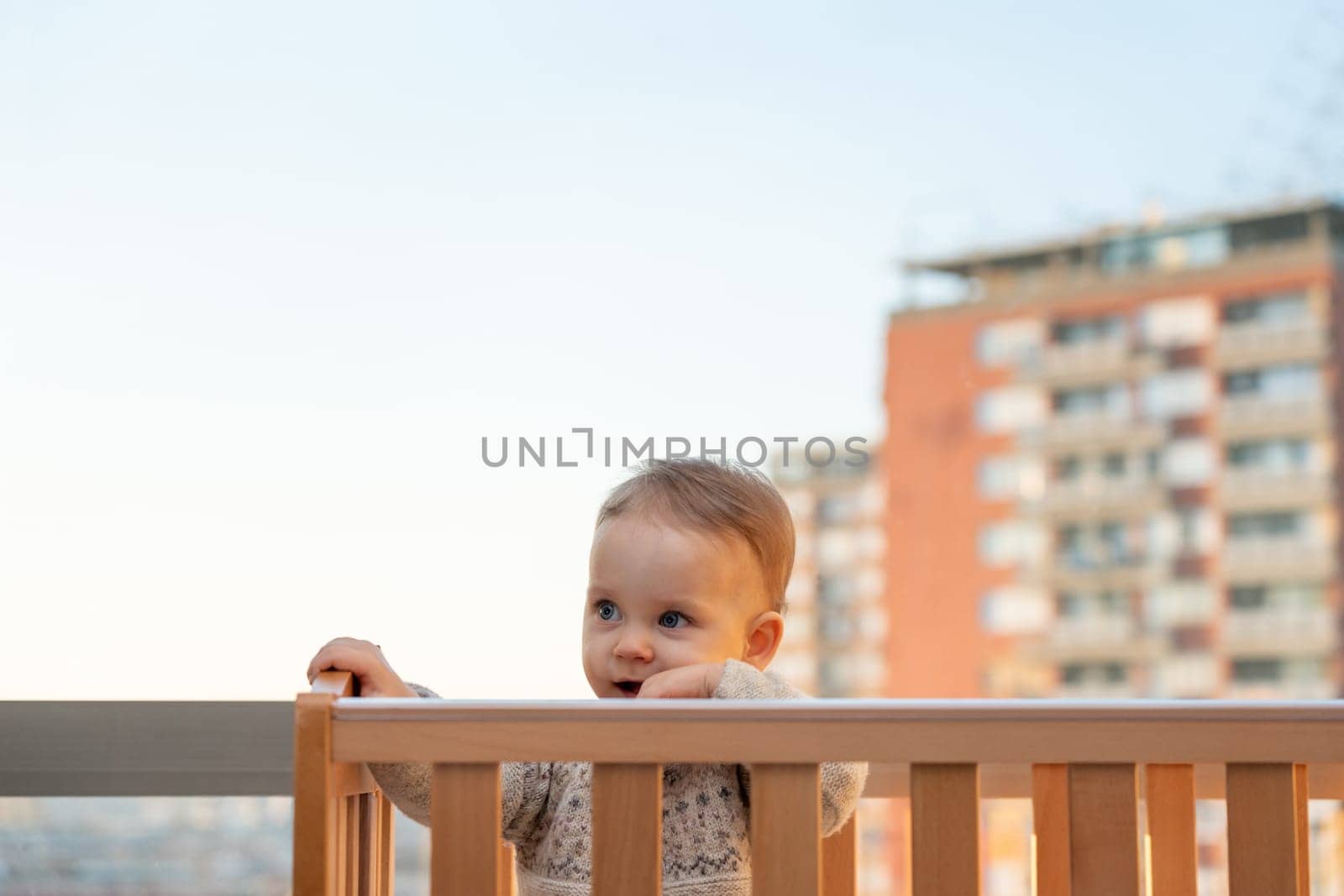 smiling baby looks out of the crib against the backdrop of a city landscape.