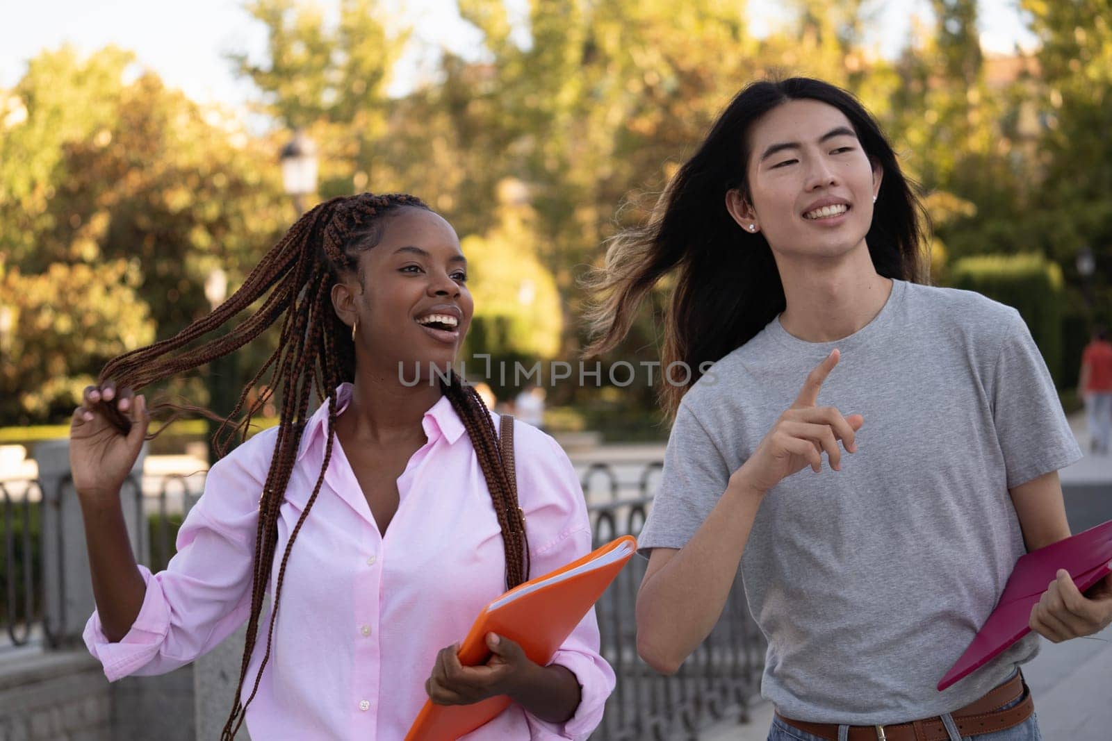 Multiethnic couple of students smiling and pointing with the finger where to go by papatonic