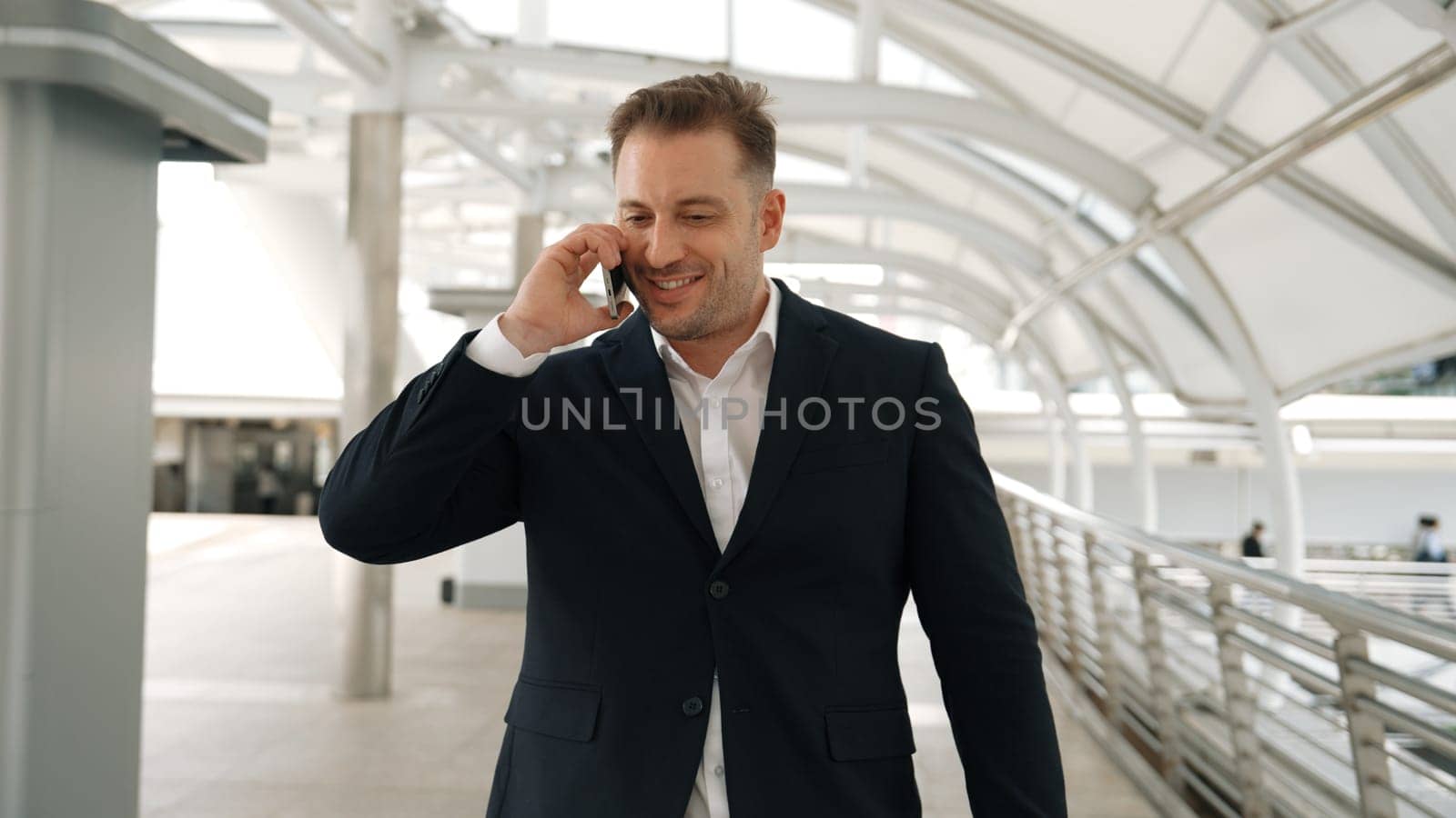 Smart caucasian businessman calling his colleague to plan financial strategy while walking to workplace. Front view of manager using mobile phone to communicate with marketing team. Lifestyle. Urbane.