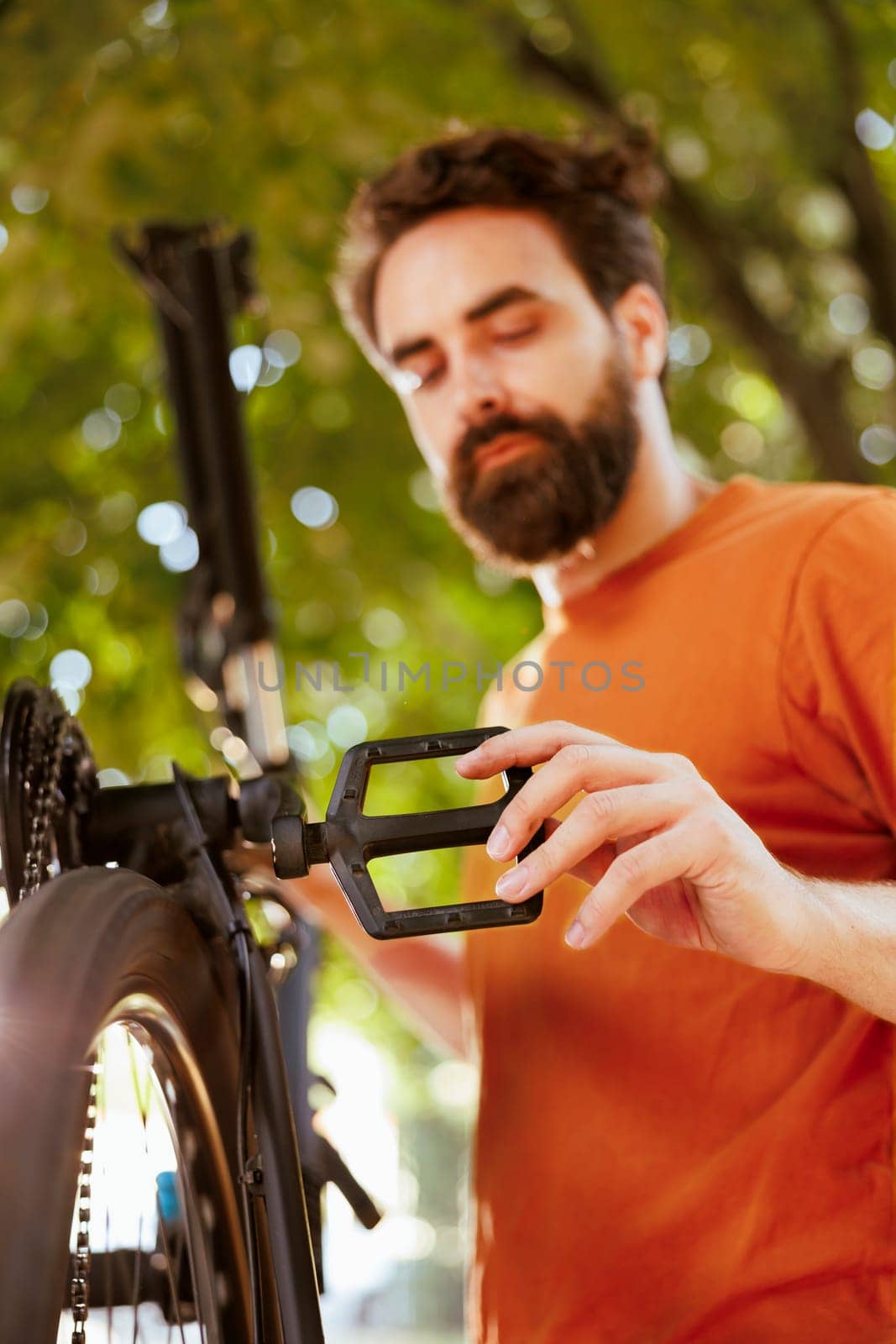 Sports-loving dedicated man repairing bicycle parts using professional tools in home yard. Healthy caucasian male cyclist assessing and mending damaged bicycle as summer activity.