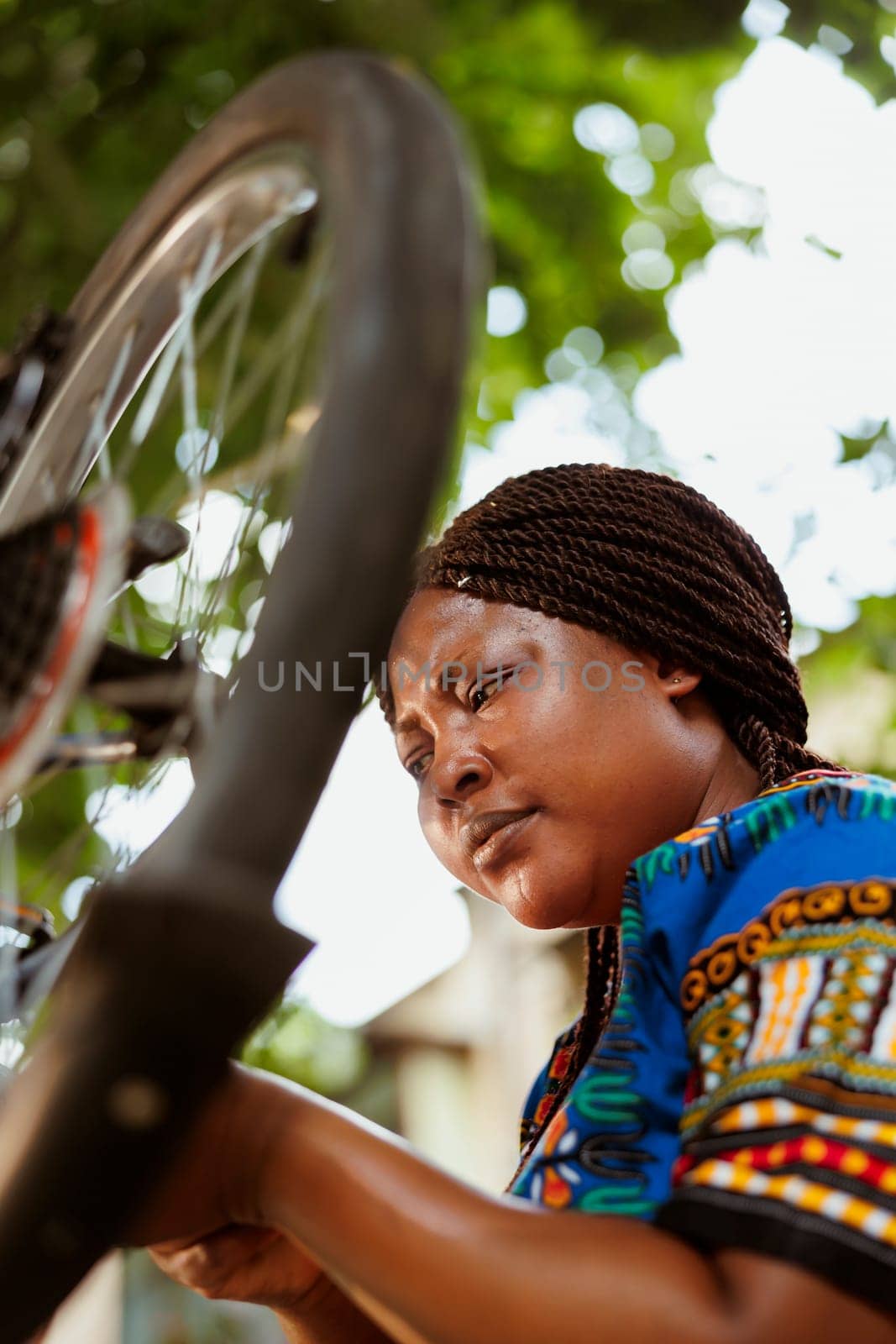 Active african american female working on broken bike rubber wheel with professional equipment in home yard. Committed sporty black woman servicing bicycle outside for summer leisure cycling.
