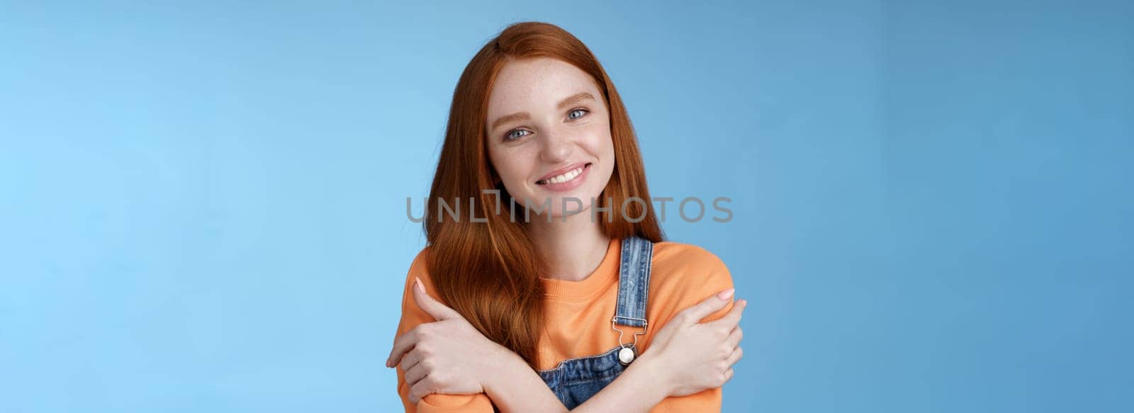 Lifestyle. Tender silly redhead girl standing blue background smiling joyfully hugging arms crossed body feel chilly grinning delighted talking boyfriend romantic date asking lend jacket cold summer evening.