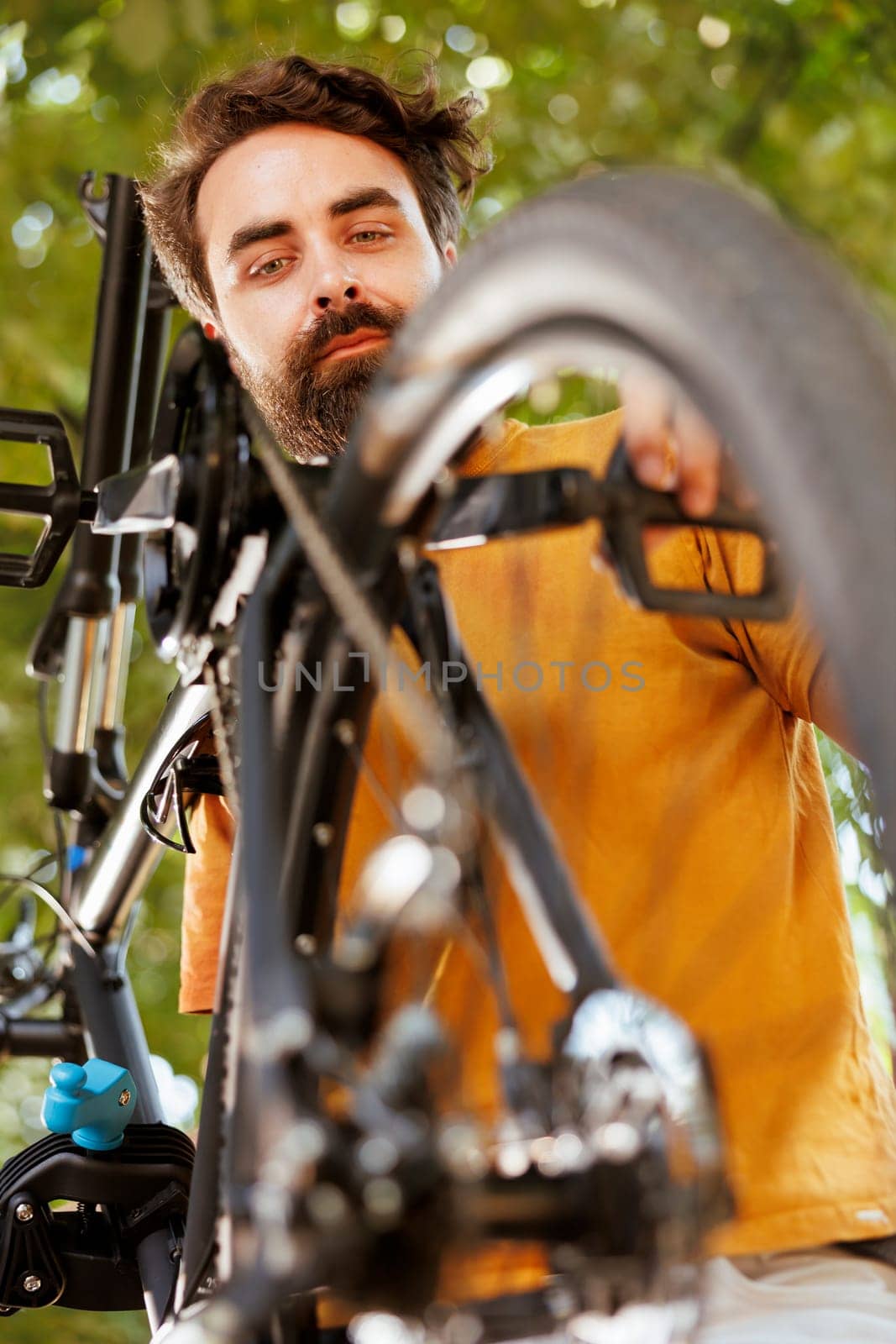 Sports-loving man inspecting bike pedal by DCStudio