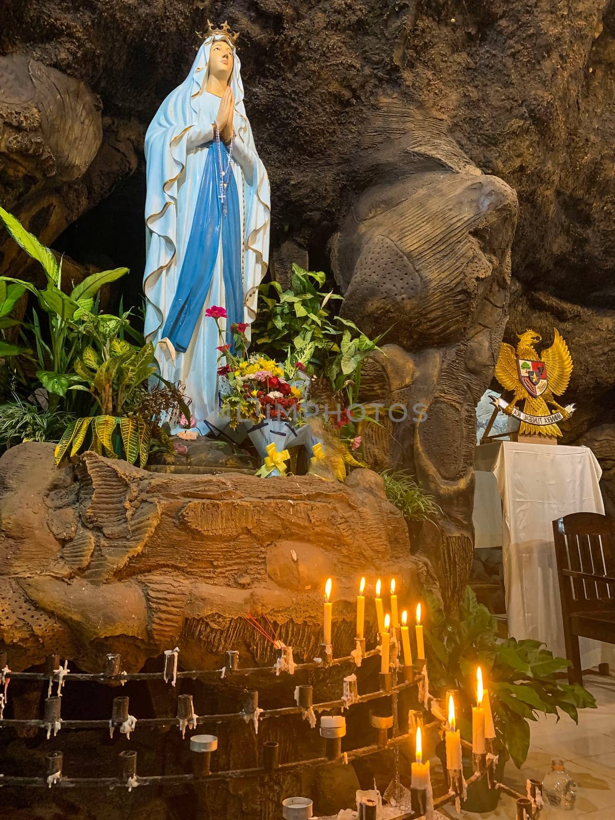 Statue of Holy Virgin Mary in Roman Catholic Church, in the cave of virgin mary, in a rock cave chapel Catholic Church with tropical flowers around in the asian