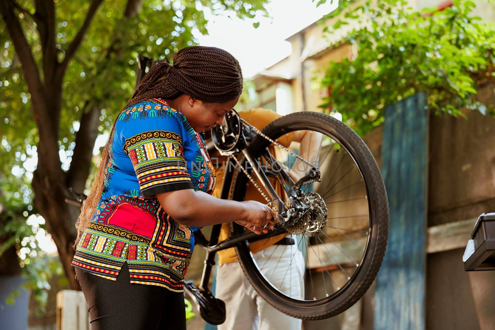 Black woman outdoors holding and fixing bicycle wheel with professional equipments. Young african american woman repairing broken bike tire with work tools in yard.