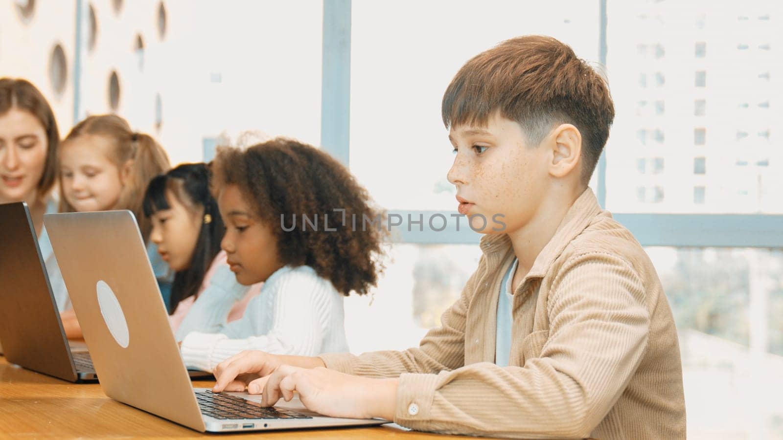 Boy playing laptop with multicultural friend learning prompt at STEM technology class. Multicultural student study about engineering code and programing system with blurring background. Erudition.