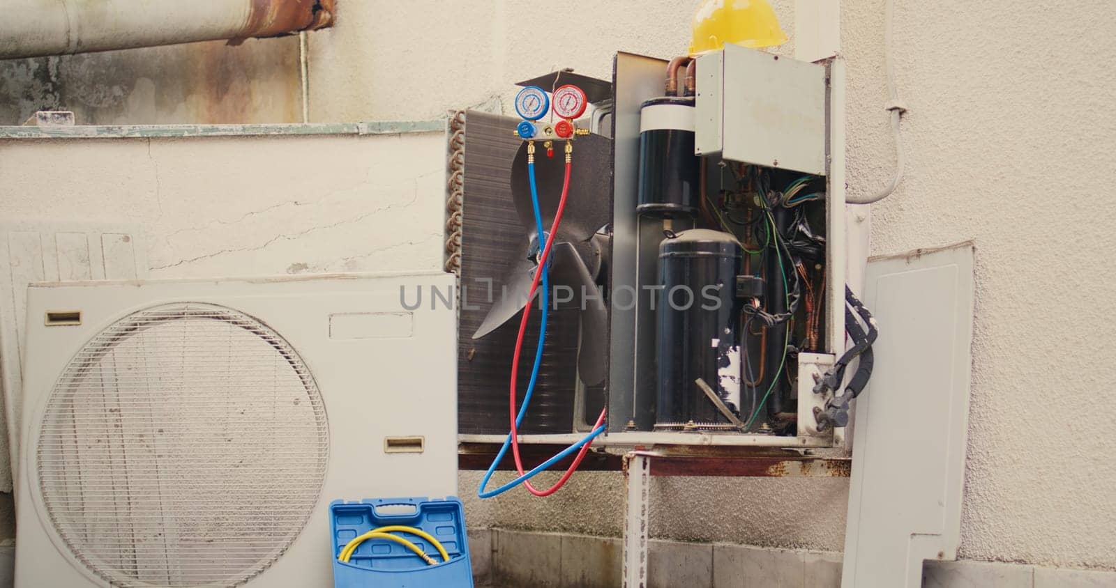 Revealing handheld camera shot of broken outdoor air cooling unit in need of fixing, with malfunctioning electric internal parts and wiring. Air conditioner not working anymore, ready to be fixed