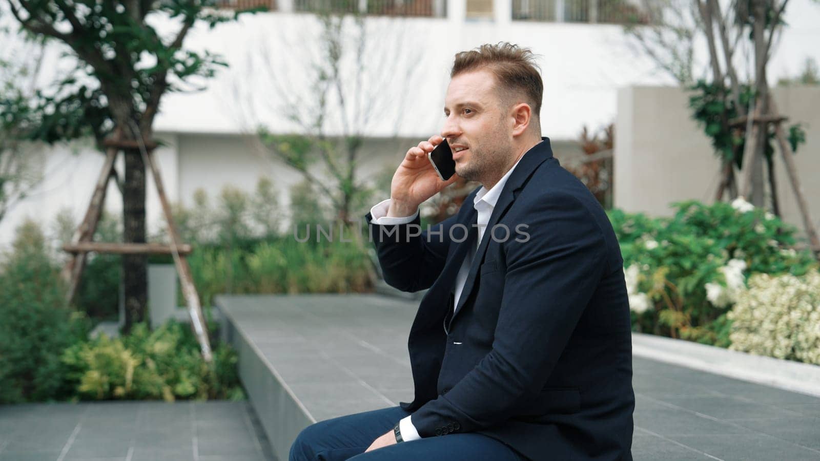 Side view of businessman sitting at park while talking to investors about marketing strategy. Caucasian executive manager looking increasing sales or successful project at eco city. Lifestyle. Urbane