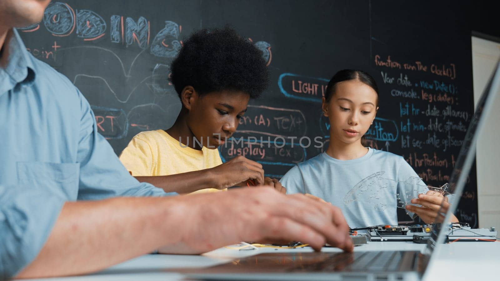 Young student fixing controller while teacher programing engineering code at STEM class. Closeup of instructor hand typing computer while smart girl using electronic tool and blackboard. Edification.