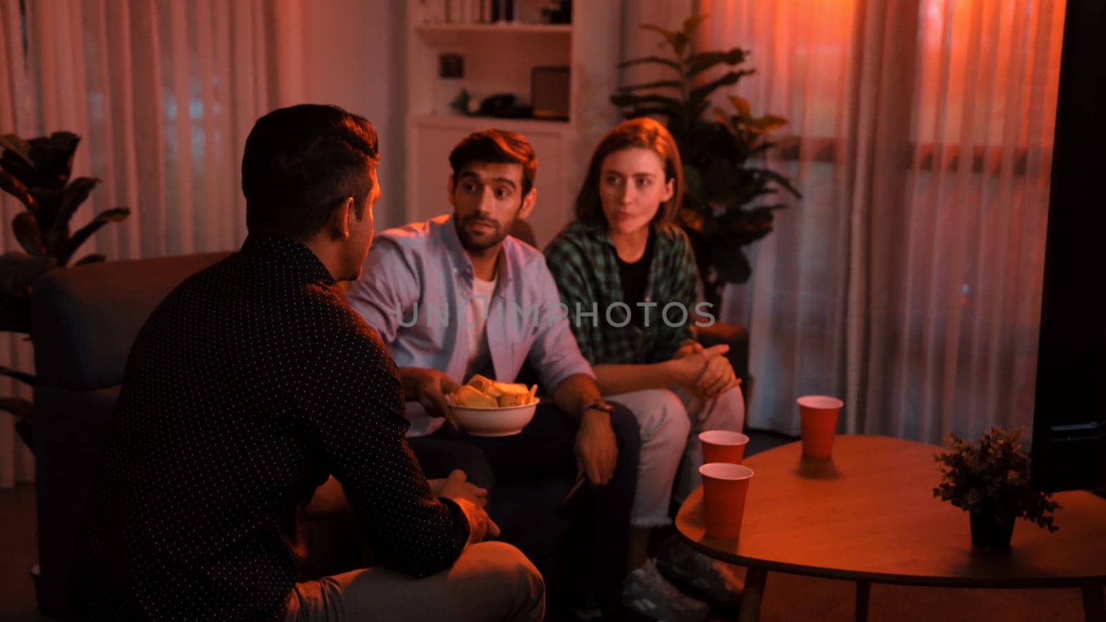 Top view of caucasian father and relaxed mother watching movie while eating snack with friend. Happy family with colleague looking at television while dad hold snack bowl at living room. Convocation.