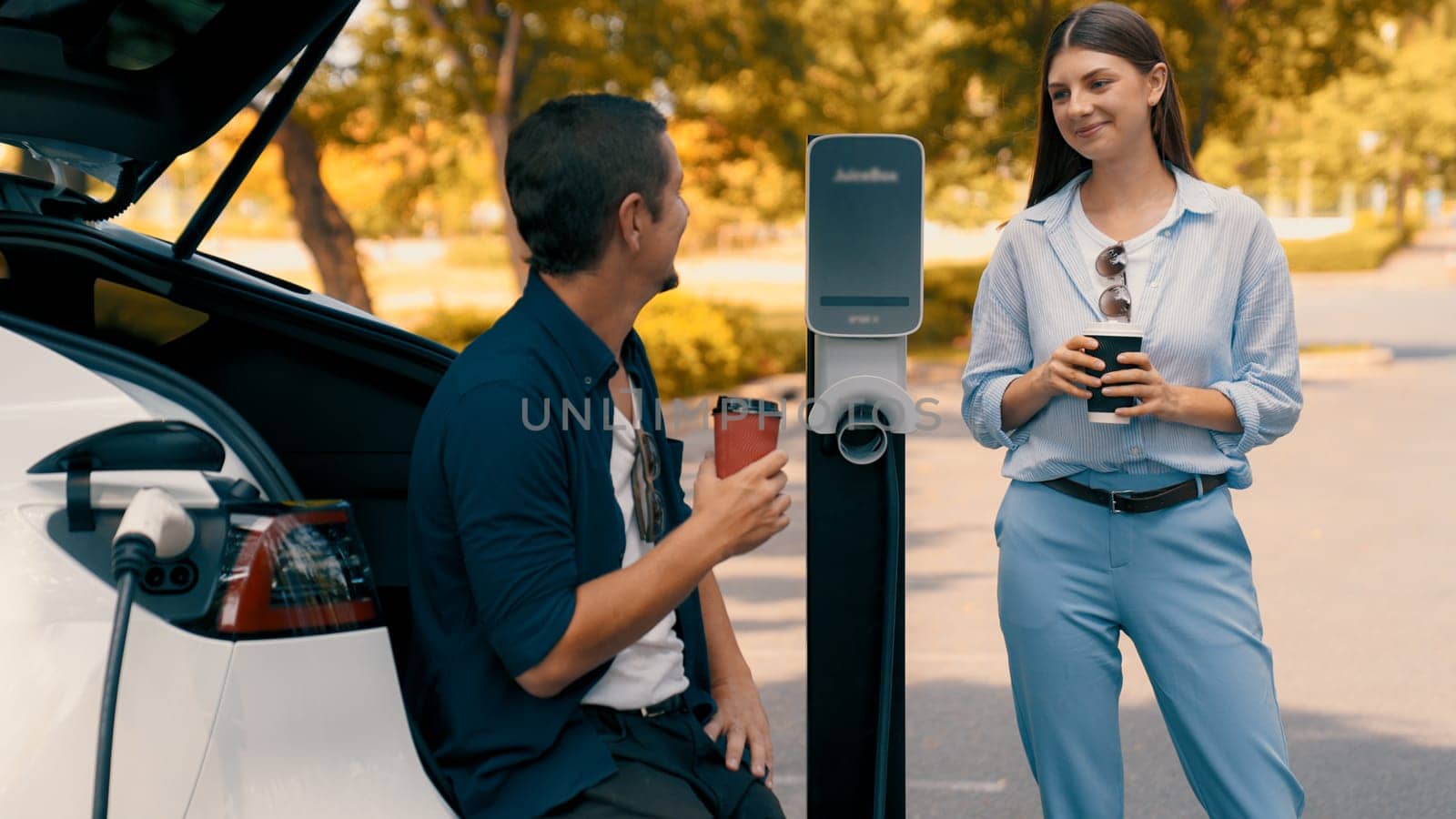 EV car recharging electricity for battery by lovey couple on road trip. Exalt by biancoblue