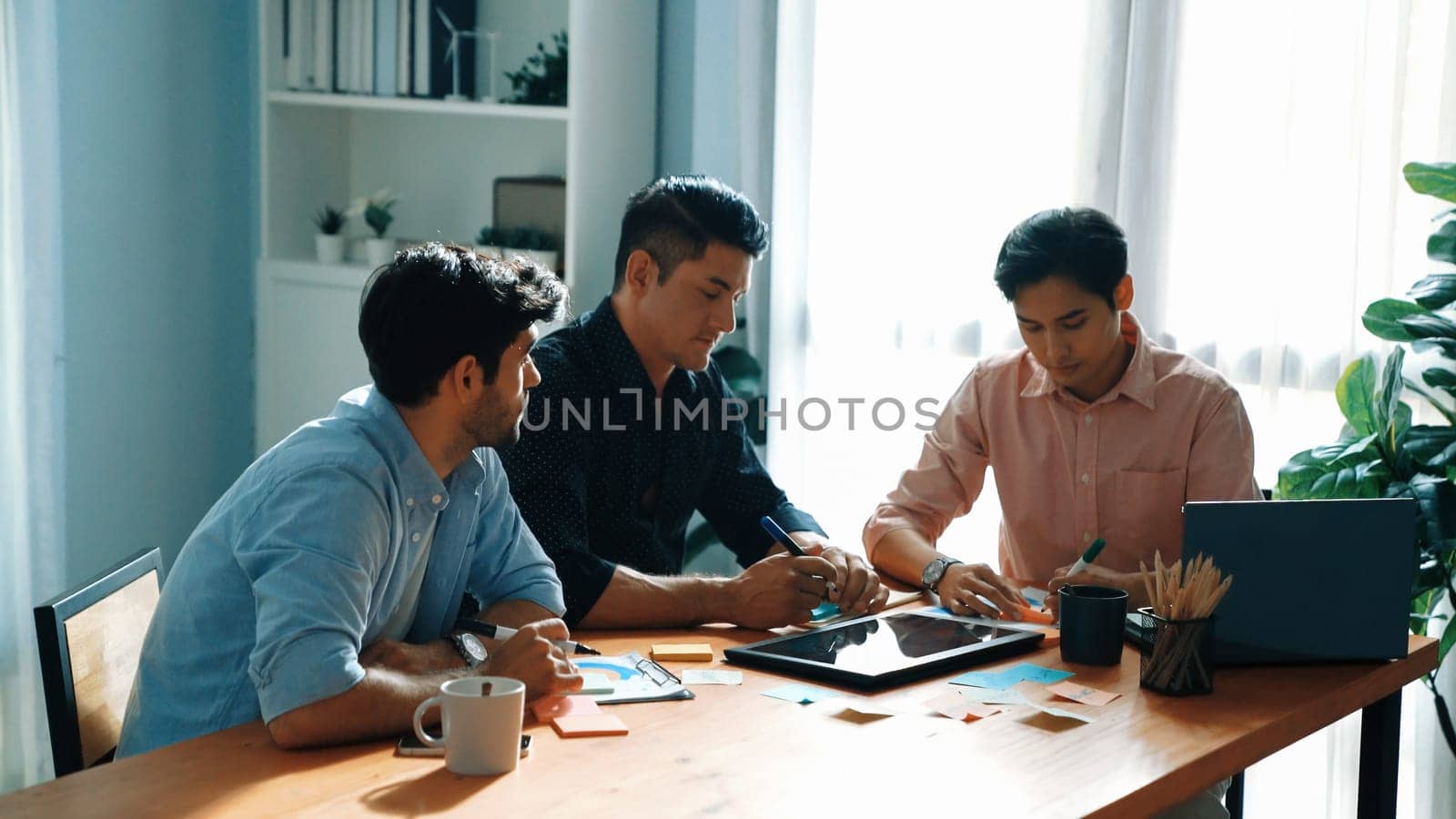 Group of diverse people sharing idea while writing at sticky notes. Professional smart business team brainstorming idea and planning strategy for startup project while wear casual outfit. Convocation.