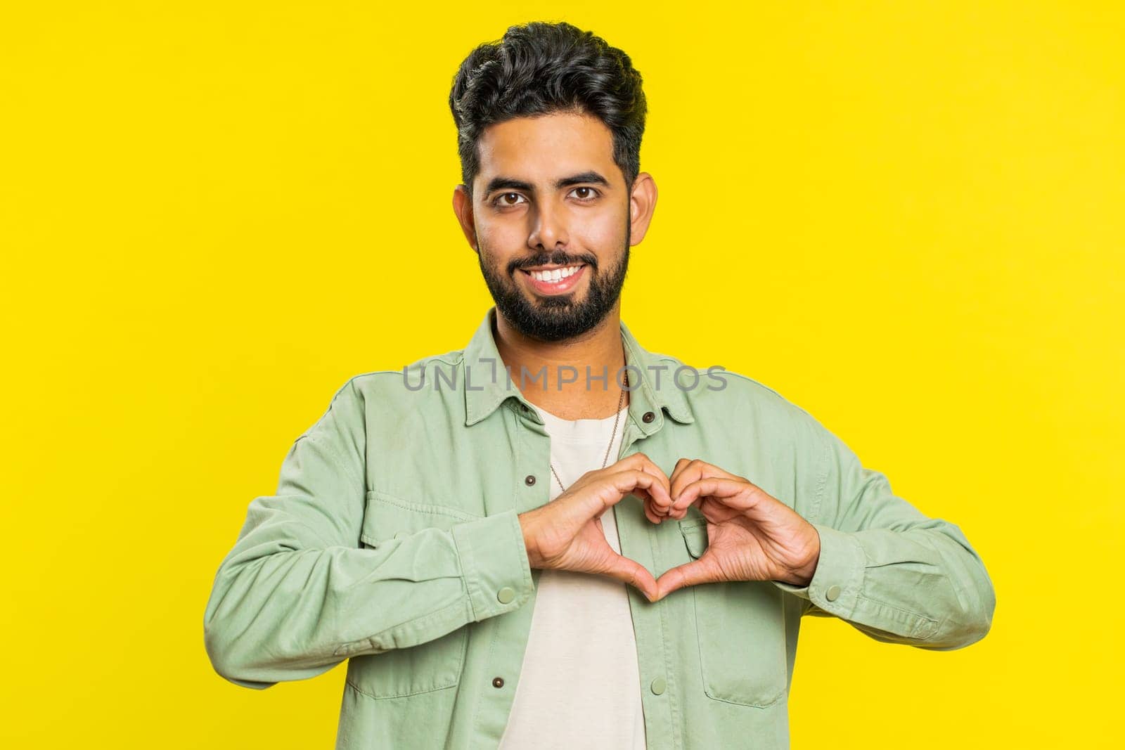 Smiling handsome man makes heart gesture demonstrates love sign expresses good feelings and sympathy by efuror