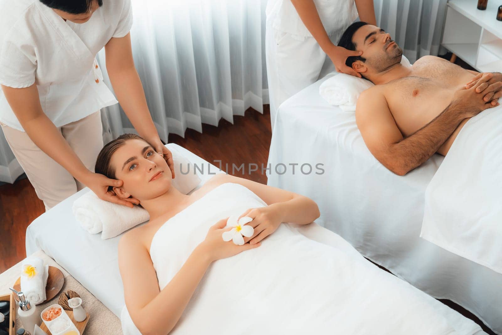 Caucasian couple enjoying relaxing anti-stress head massage and pampering facial beauty skin recreation leisure in dayspa modern light ambient at luxury resort or hotel spa salon. Quiescent