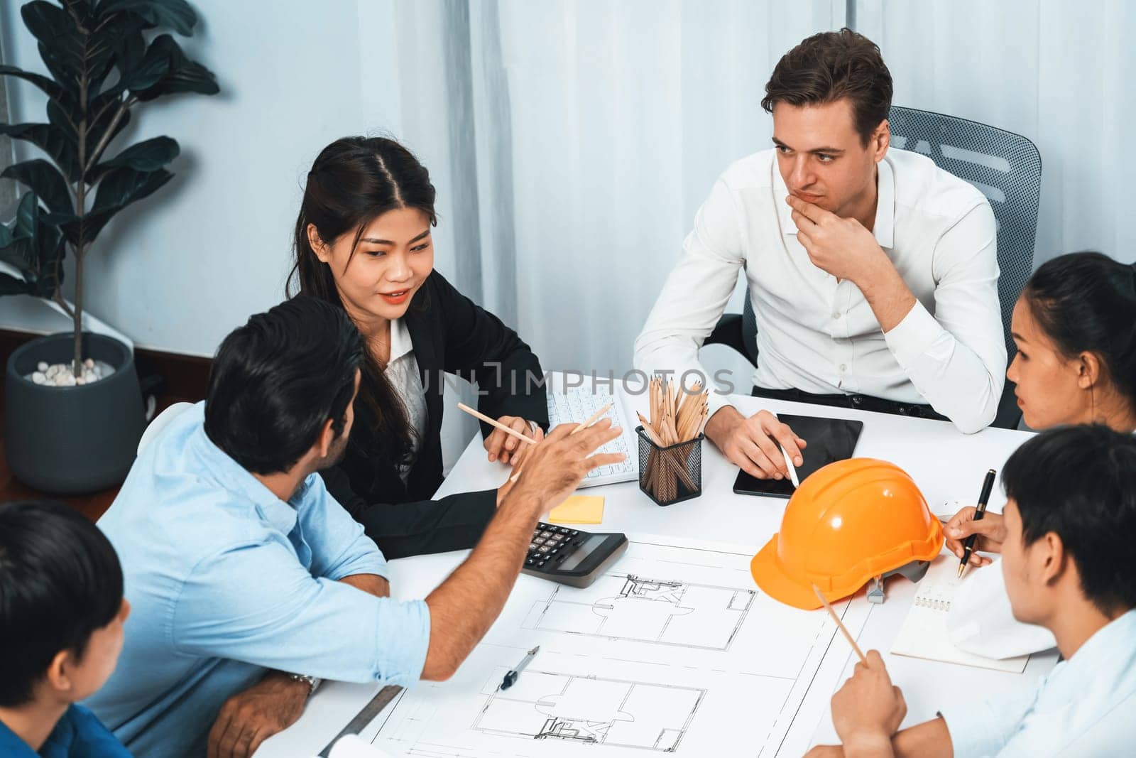 Diverse group of civil engineer and client working together on architectural project, reviewing construction plan and building blueprint at meeting table. Prudent