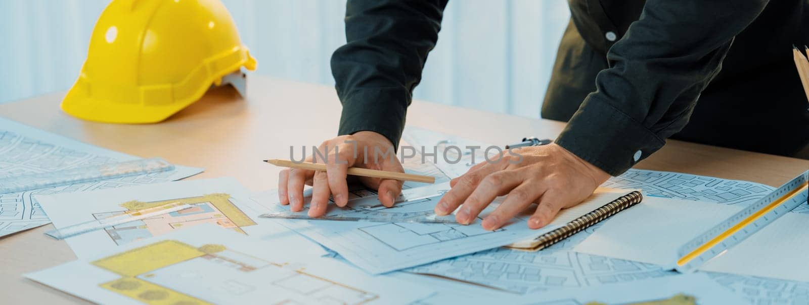 Professional engineer measuring the blueprint. Professional engineer working architectural project at studio on a table with yellow helmet and architectural equipment scatter around. Delineation.