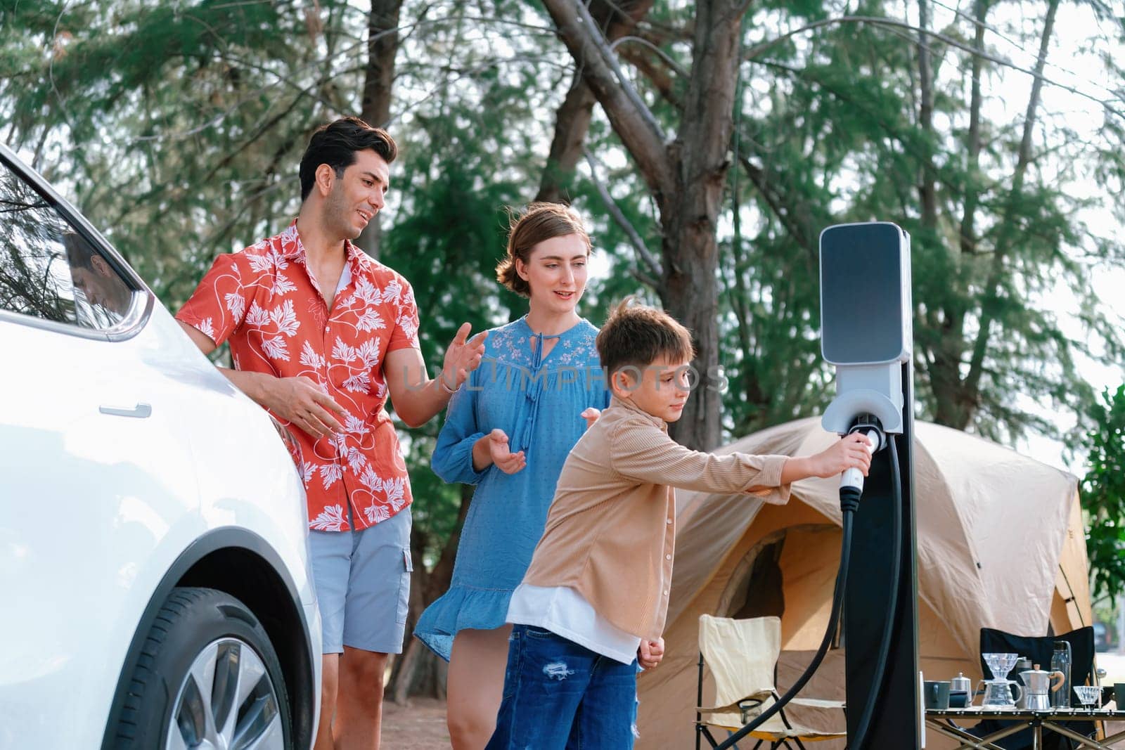 Outdoor adventure and family vacation camping in nature travel by eco friendly car for sustainable future. Lovely family recharge EV car with EV charging station in campsite. Perpetual