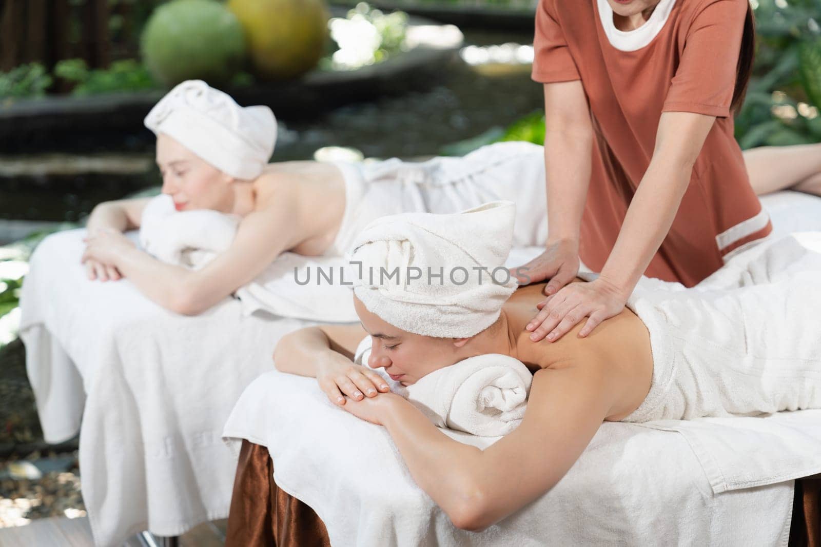 A portrait of two young attractive woman lie on bed during having back massage by a professional masseur at outdoor surrounded by peaceful natural environment. Healthy and beauty concept. Tranquility.