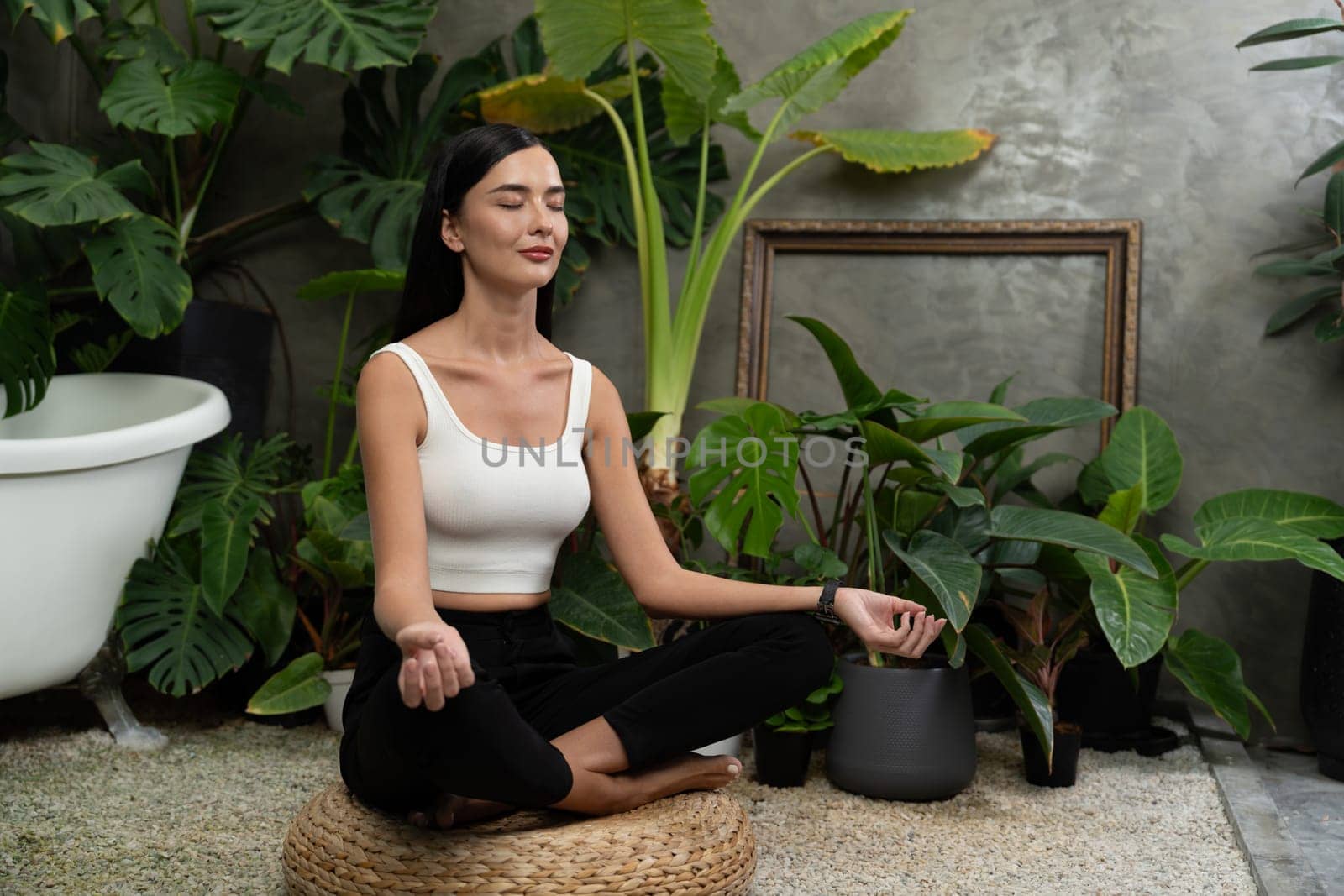 Young woman doing morning yoga and meditation in natural garden with plant leaf, enjoying the solitude and practicing meditative poses. Mindfulness activity and healthy mind lifestyle. Blithe