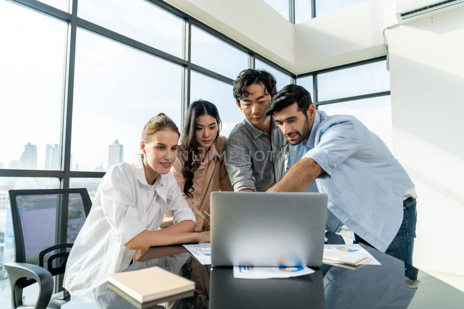 Asian project manager uses laptop displayed data analysis while professional business team brainstorming marketing idea at business meeting. Working together,sharing idea, planing strategy. Tracery.