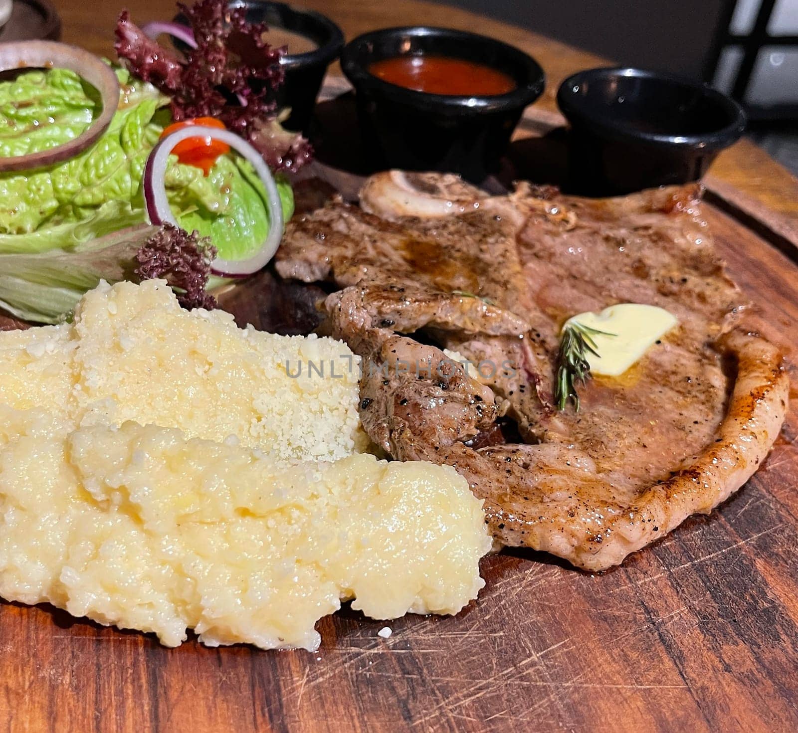 Juicy beef steak with salad and mashed potato along with pepper corn sauce served on wooden plate wooden stone table. Top view on a restaurant