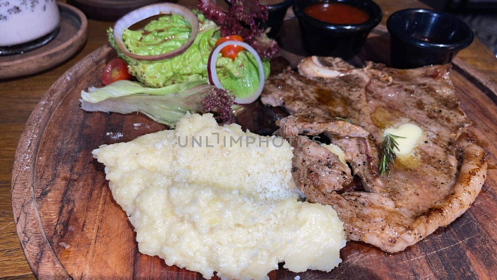 Juicy beef steak with salad and mashed potato along with pepper corn sauce served on wooden plate wooden stone table. Top view on a restaurant
