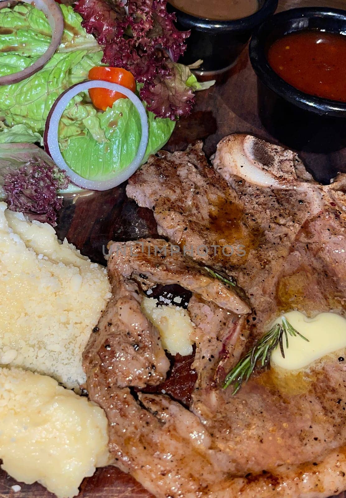 Juicy beef steak with salad and mashed potato along with pepper corn sauce served on wooden plate wooden stone table. Top view on a restaurant
