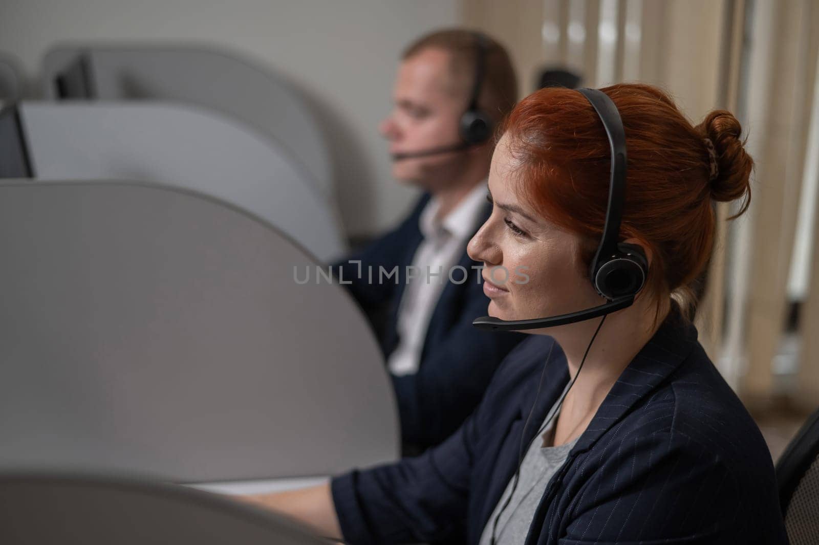 Two serious call center employees are talking with clients. Man and woman working with headsets in office