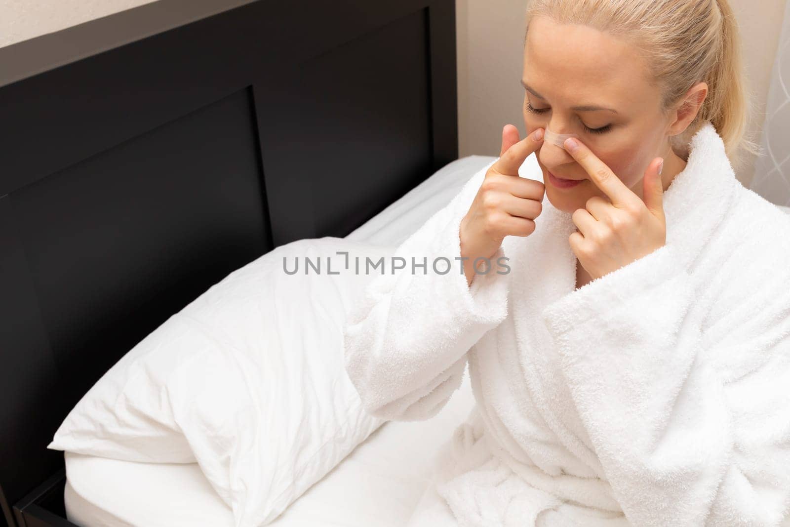 White Woman Applies Nasal Strip on Nose Before Going To Bed, Sitting on Bed. Stop Drug-free, Snoring, Sleeping Apnea Solution. Copy Space. Adhesive Bandage For Better Healthy Breathing. Horizontal. by netatsi