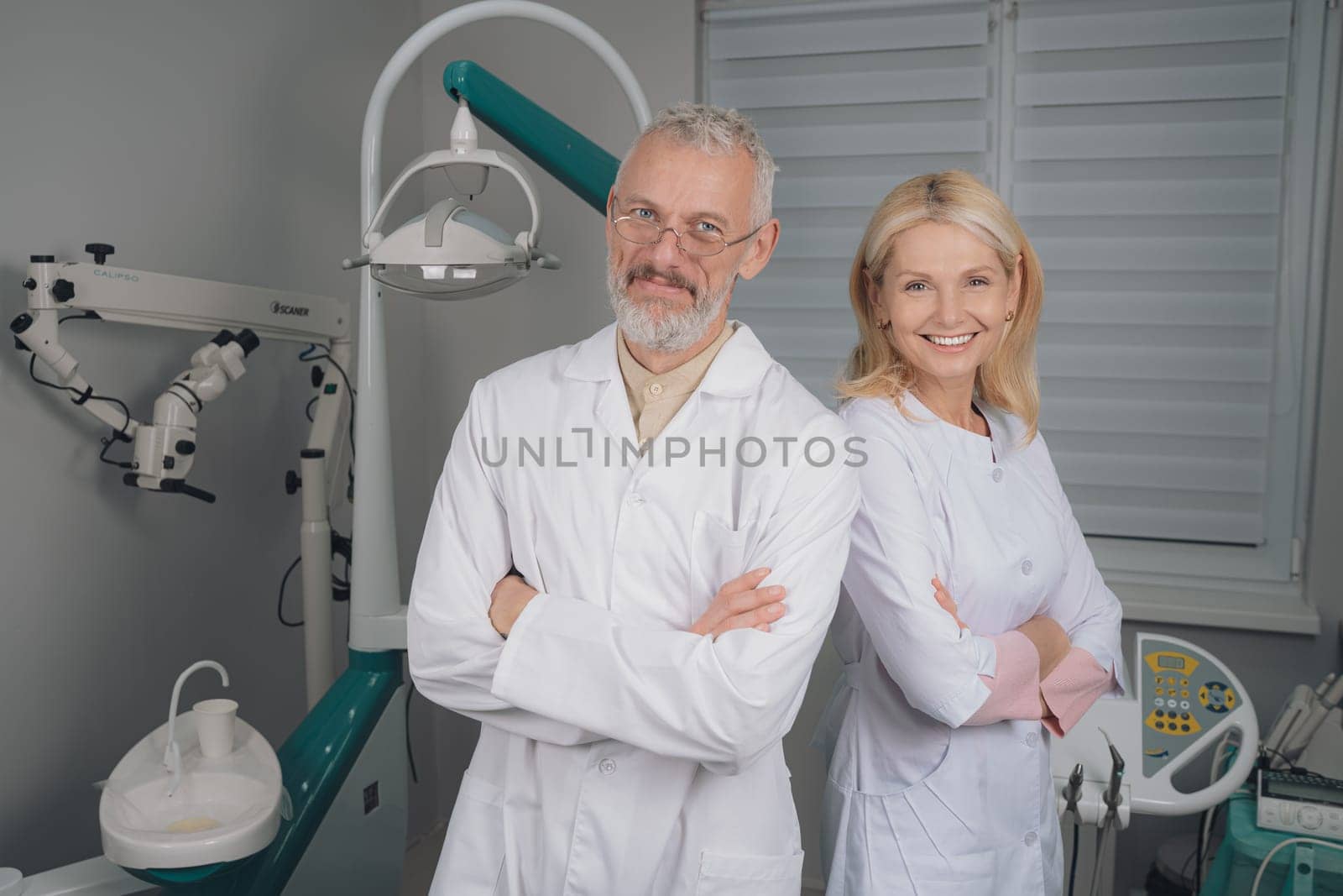 Male and female dental doctors wearing face sitting at his clinic. by Сookiestock