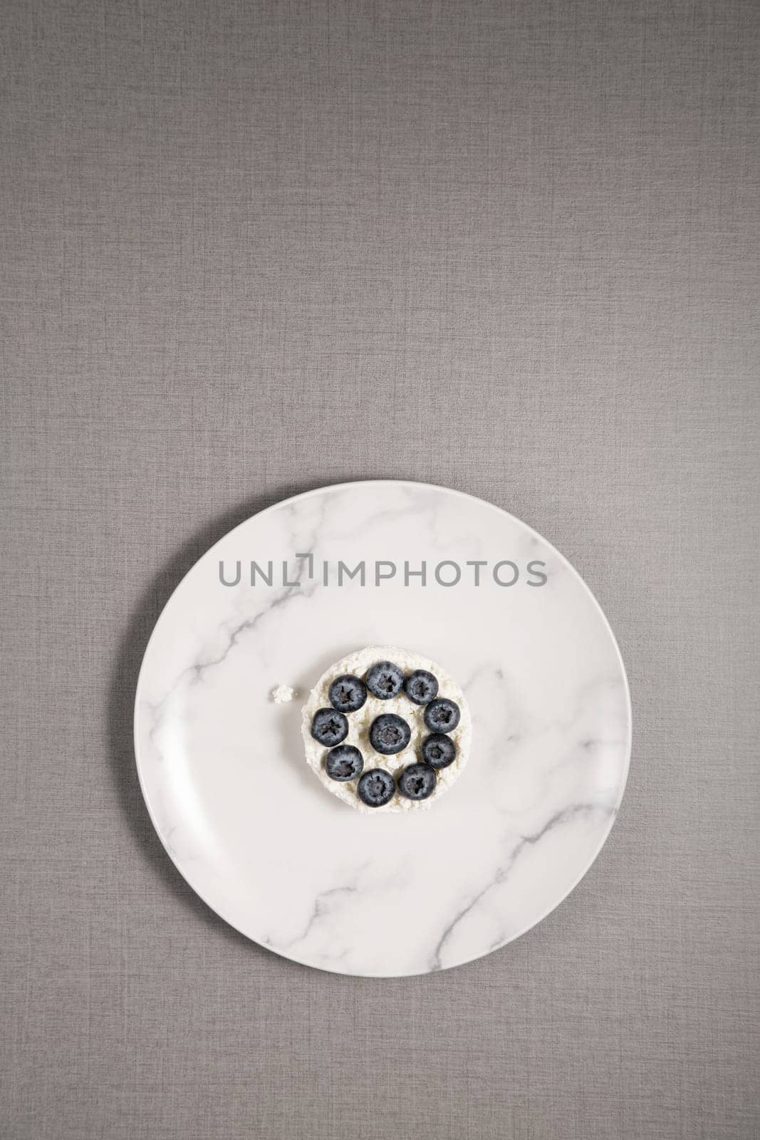 Cottage cheese with blueberries in a plate on a gray background, with copy space for text by NataliPopova