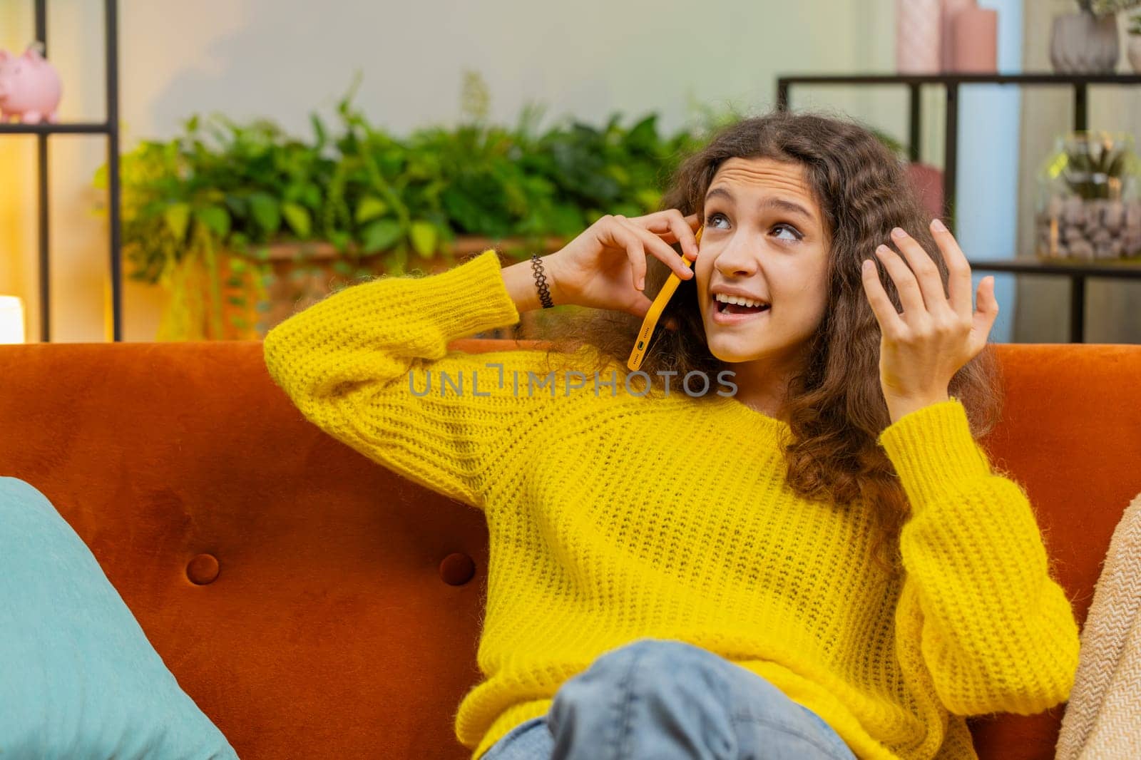 Phone call, good news, gossip. Happy surprised 14-15 years child girl in pleasant conversation on smartphone, enjoying talking with friend. Teenager Caucasian female kid at home room apartment on sofa