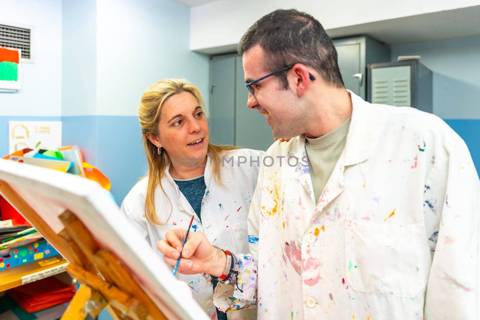 Teacher of a painting class talking to a disabled student in a center of people with special needs