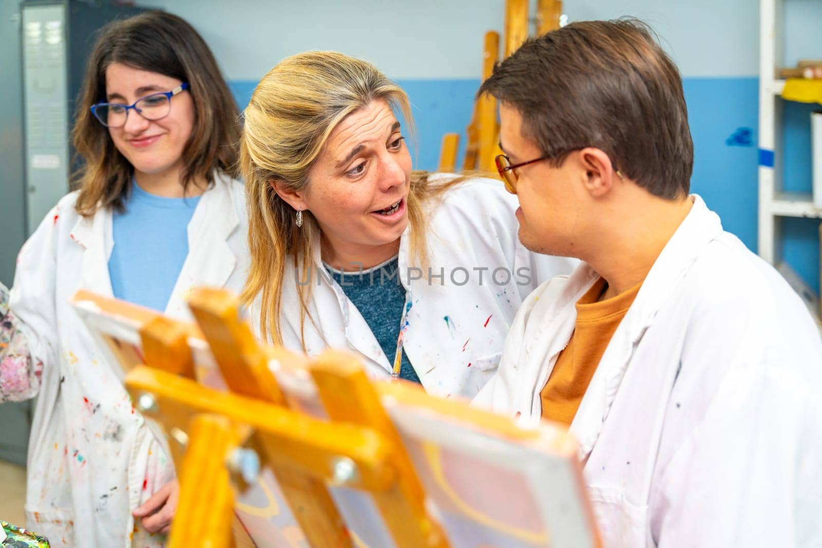Art teacher talking to a man with down syndrome while painting on canvas