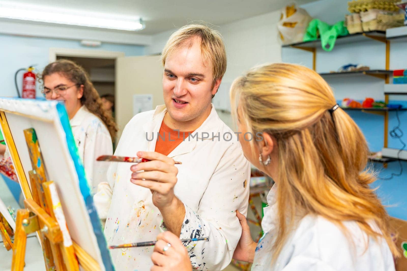 Disabled man using brush to paint next to a teacher in a class