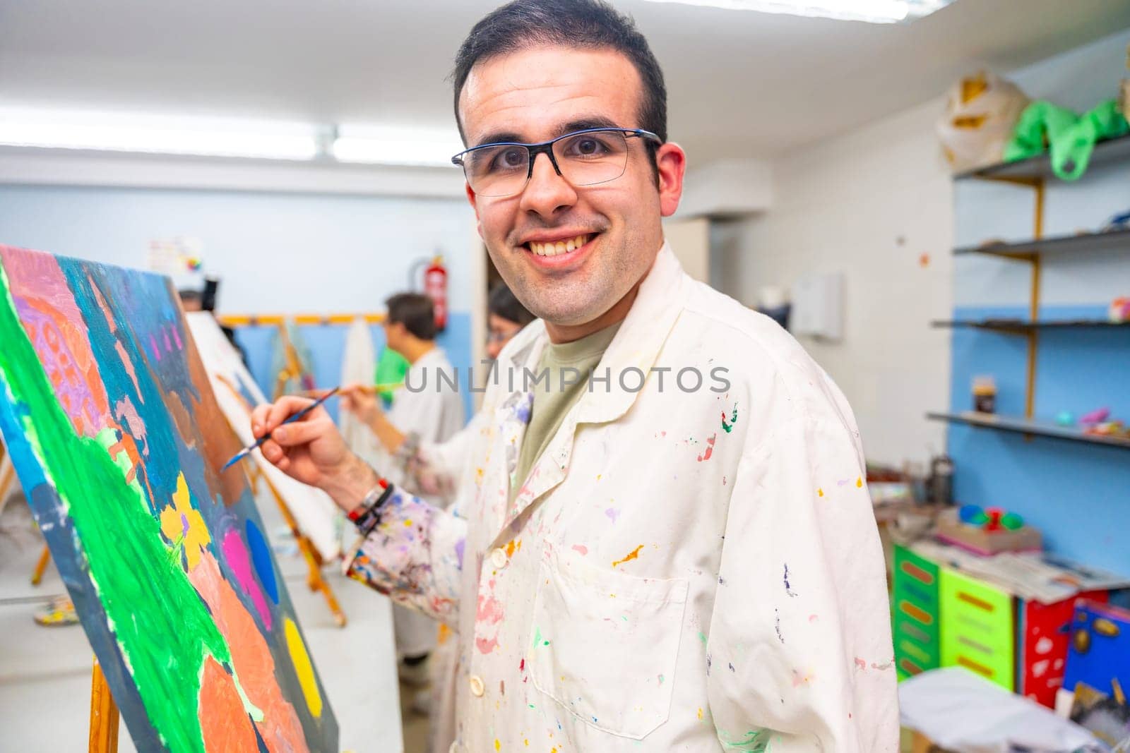Disabled man looking at camera and smiling happy while painting on canvas