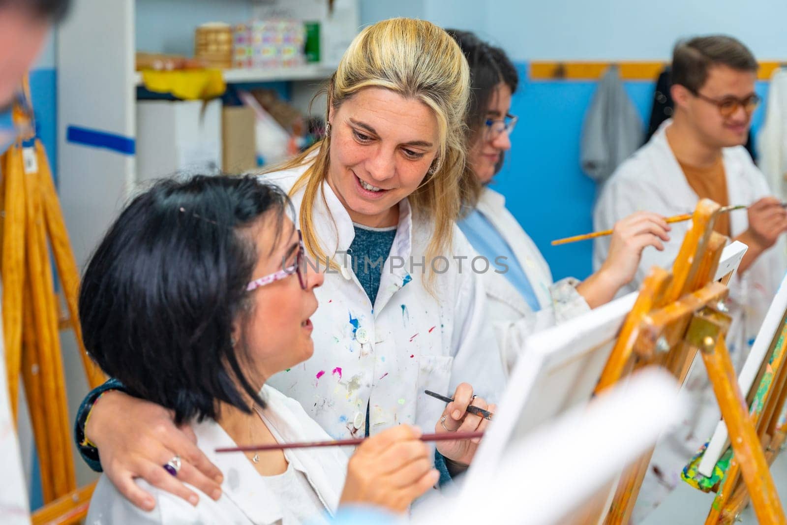 Teacher encouraging a disabled woman during painting class with other people