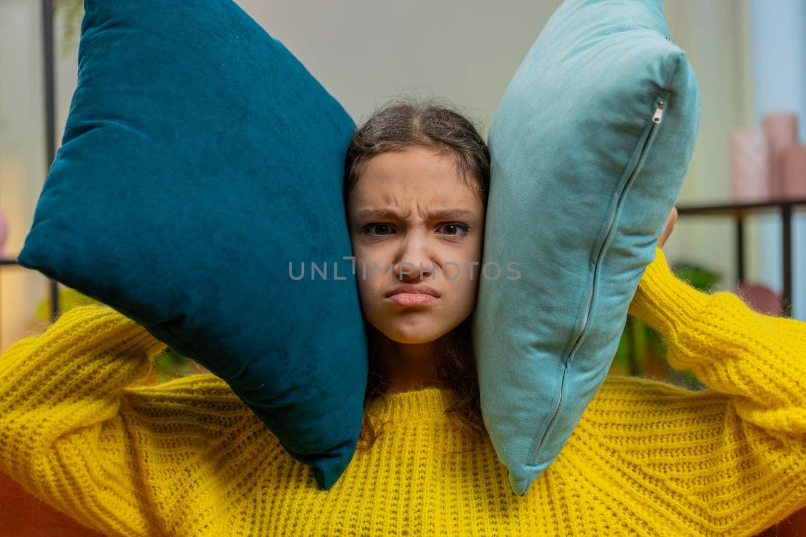 Repair work at neighbors. Irritated angry sad child girl kid cover ears with pillows annoyed by noisy loud music suffers headache wishes silence. Thin walls at home flat without sound insulation