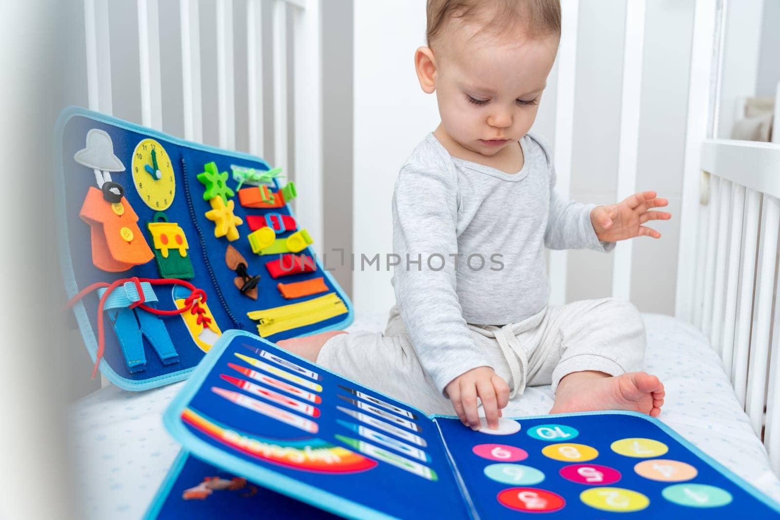 Baby playing with montessori quiet book sitting in a crib. Concept of smart books and modern educational toys by Mariakray