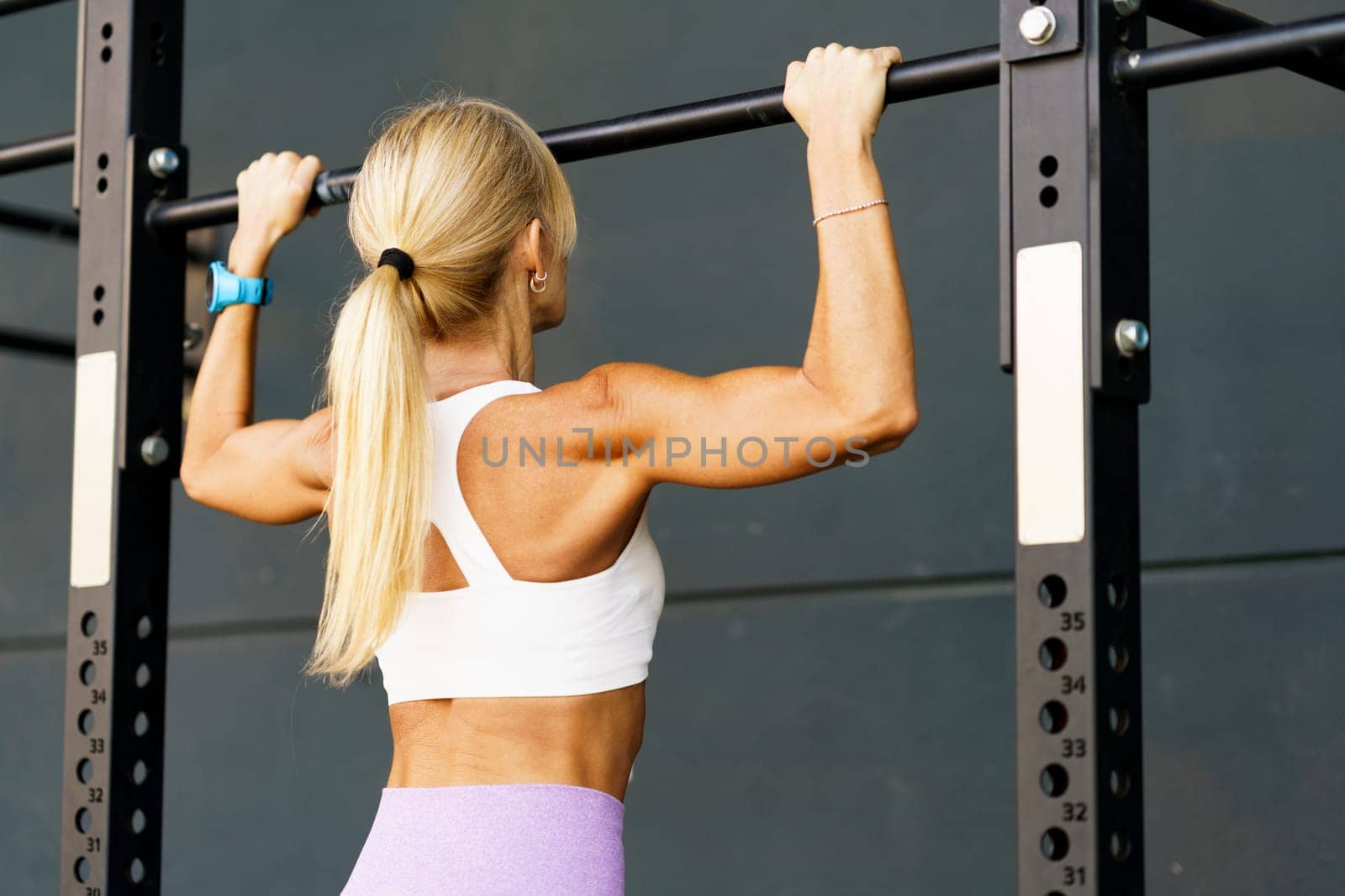 Unrecognizable woman doing pull ups on bar in fitness club by javiindy