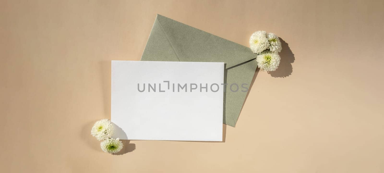 Beautiful little white flowers on postal green envelope on beige background, empty paper note copy space for text, spring time, greeting card for holiday. Flower delivery concept