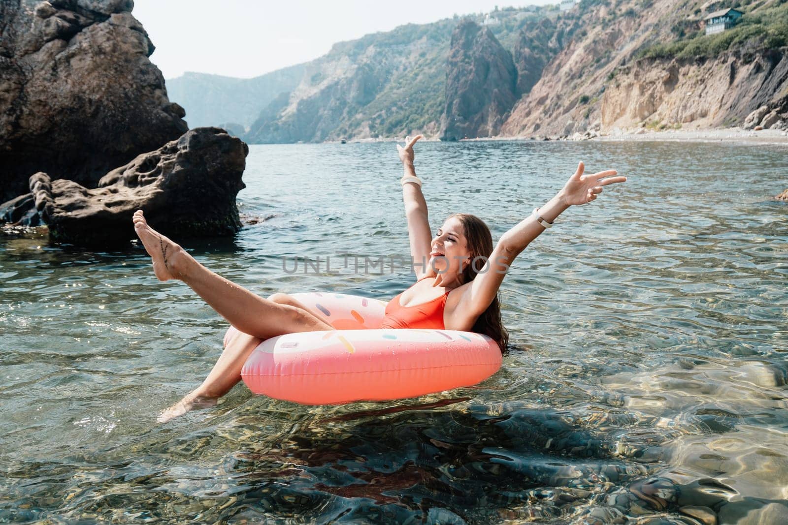 Woman summer sea. Happy woman swimming with inflatable donut on the beach in summer sunny day, surrounded by volcanic mountains. Summer vacation concept