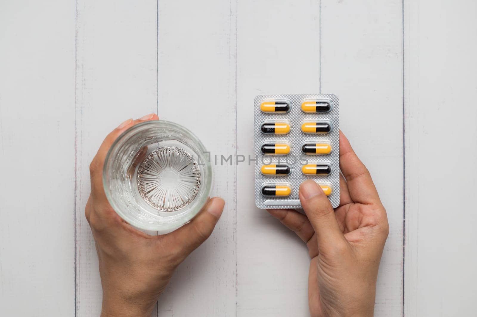 Healthcare Concept with Hand Holding Water and Pills on White Wooden Table by iamnoonmai